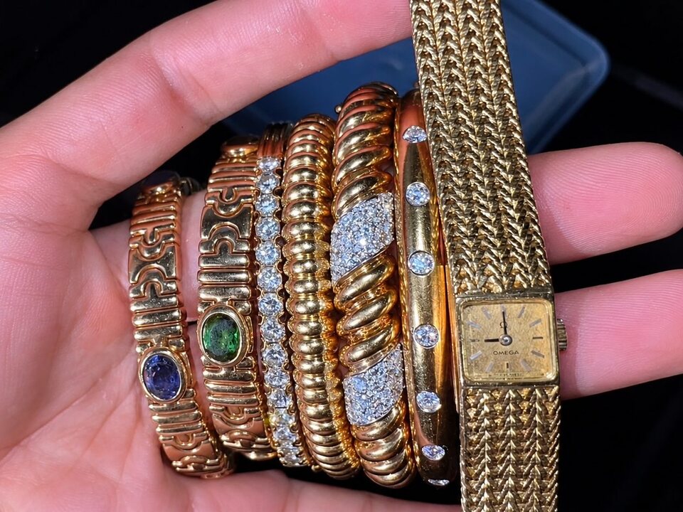 A hand holding a stack of gold bangles and bracelets with a vintage gold wristwatch